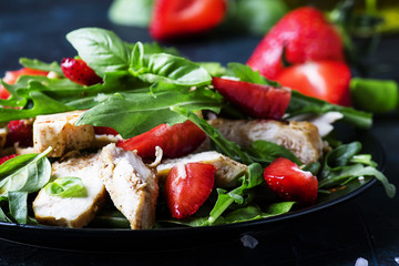 Grilled chicken salad, fresh strawberries and spicy arugula, dark background, selective focus