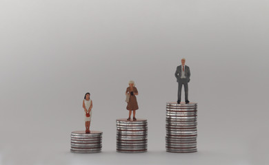 A miniature man and two miniature women standing on a stack of coins of different heights. The...