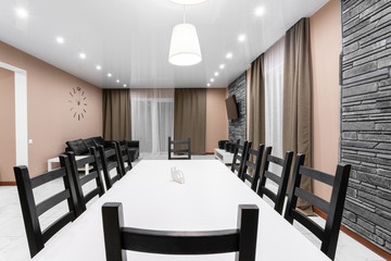 dining table for ten people. Modern minimalism style drawing-room interior. Simple and inexpensive living room with kitchen. interior light evening