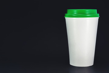 white plastic coffee cup with green lid on black background, front view with copy space