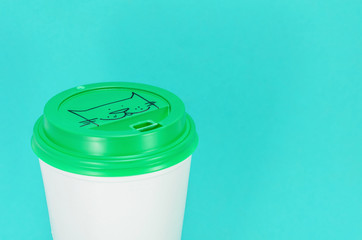 white plastic coffee cup with green lid on a blue background, view from above with copy space