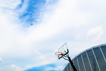 Basketball court on rooftop, clear blue sky with white cloud, airplane flying over © Croc80