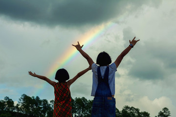 Fototapeta na wymiar Children playing under cloudy sky with rainbow.