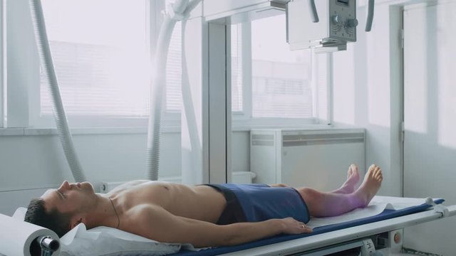 In the Hospital, Man Lying in Bed during X-Ray Machine Scanning Procedure. Scanning for Fractures, Broken Limbs, Injuries, Cancer or Tumor. Shot on RED EPIC-W 8K Helium Cinema Camera.