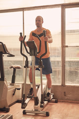 one young man, wearing sport clothes, traning on elliptical, old beaten up gym indoors.