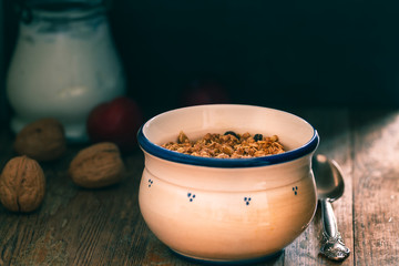 Bowl with Granola or Muesli and a jar of milk or plain yogurt with a spoon on a vintage wood background. Healthy breakfast composition