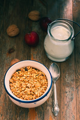 Bowl with Granola or Muesli and a jar of milk or plain yogurt with a spoon on a vintage wood background. Healthy breakfast composition