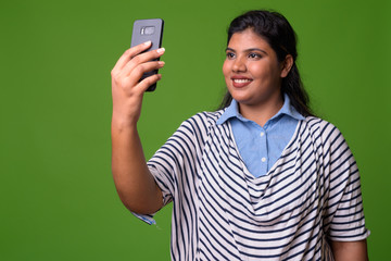 Young overweight beautiful Indian businesswoman against green background
