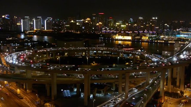 Aerial freeway busy city rush hour heavy traffic jam highway Shanghai at night,timelapse,nanpu overpass interchange,Brightly lit urban building skyline,busy shipping sailing on huangpu river.