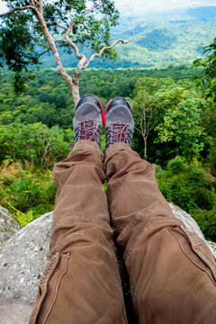 Legs of a men resting in boots for mountain tracking against the backdrop of mountains and valleys with noisy clouds Hiking boots in the mountains. Resting time. Freedom concept