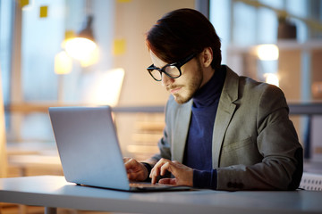 Hard-working young entrepreneur in eyeglasses preparing visual presentation for business partners...