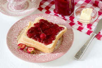 Breakfast of bread toasts with butter and strawberry-rhubarb jam, served with tea. Rustic style.