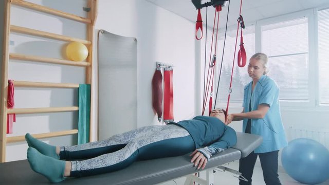 Physiotherapist Assists Female Patient with Trauma, Undergoing Rehabilitative Physiotherapy on a Special Suspension Rope System. Relieving Back Pain. Shot on RED EPIC-W 8K Helium Cinema Camera.