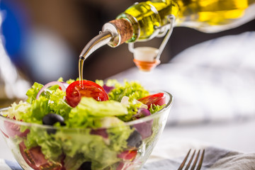 Olive oil pouring in to bowl of fresh vegetable salad