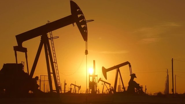 The silhouette of oil pumps in a large oil field at sunrise.