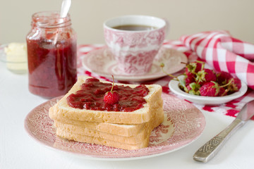 Breakfast of bread toasts with butter and strawberry-rhubarb jam, served with tea. Rustic style.