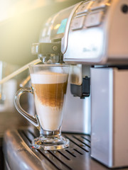 Cappuccino coffee being prepared from coffee machine into glass cup. Professional coffee brewing, hot coffee.