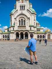 Obraz premium Young caucasian man with a map visiting Alexander Nevsky cathedral in Sofia, Bulgaria. Solo traveler concept.