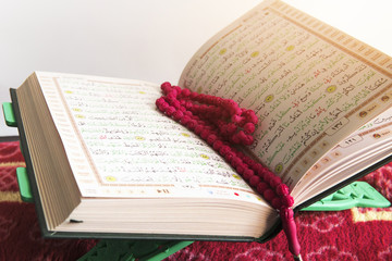 Selective focus of Holy Quran and red beads or tasbih on white background.