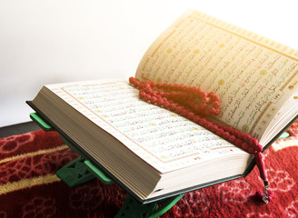 Selective focus of Holy Quran and red beads or tasbih on white background.
