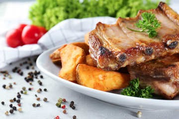 Plate with delicious grilled ribs and potato on table