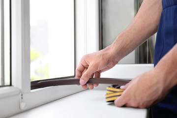 Construction worker putting sealing foam tape on window indoors