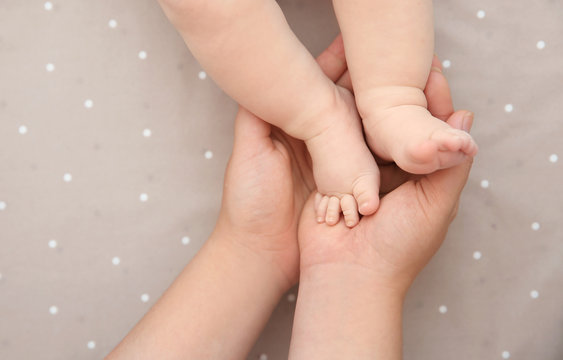 Mother holding little baby feet in hands, top view