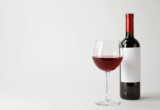 Bottle and glass with delicious red wine on white background