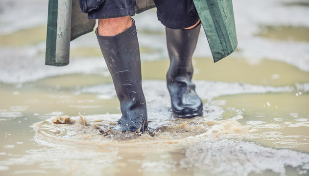 A man with black boots walks on a flooded road