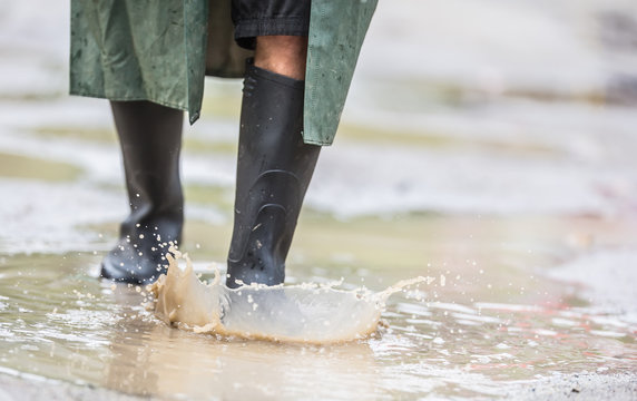 A man with black boots walks on a flooded road
