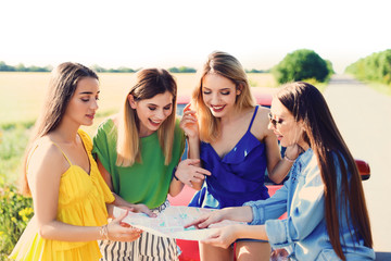 Happy beautiful young women with map standing near car in countryside