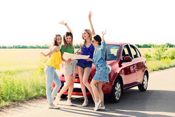 Obraz premium Happy beautiful young women with map standing near car in countryside