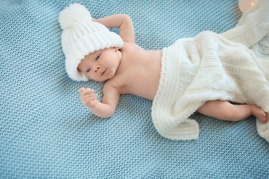 Adorable newborn baby in warm hat lying on bed, top view