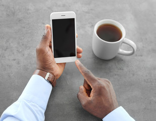 African-American man holding mobile phone with blank screen in hand at table