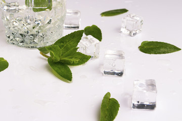Glass with refreshing water, mint leaves, water droplets and ice cubes on a light background