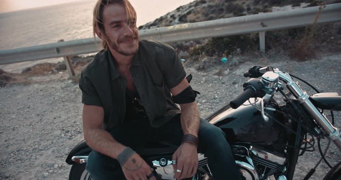 Young rebel man sitting on motorcyle by the sea
