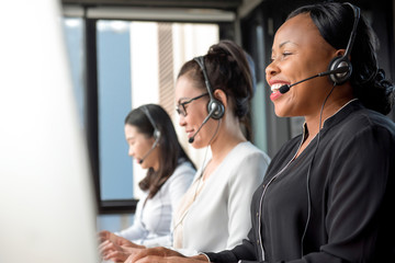 Friendly black woman wearing microphone headset working in call center with international team as...
