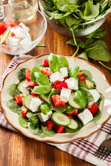 Fresh spinach salad with feta, cucumber and red paprika on a pla