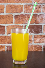 Orange juice in a cup with a tube on a wooden table and a brick wall background
