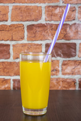 Orange juice in a cup with a tube on a wooden table and a brick wall background