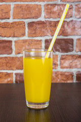 Orange juice in a cup with a tube on a wooden table and a brick wall background