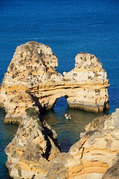Elevated view of a natural arch in the ocean with a boat to the centre, Praia da Dona Ana, Lagos, Portugal.
