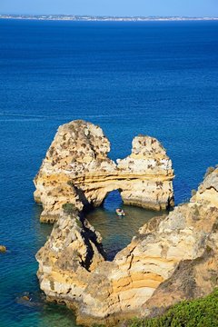 Elevated view of the coastline and a natural arch in the ocean and a boat to the centre, Praia da Dona Ana, Lagos, Portugal.