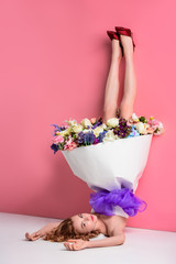 beautiful young woman with fresh flowers in dress looking at camera on pink