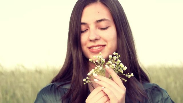Beauty girl enjoying nature outdoor, smelling wild flowers on summer field. Happy young woman romantic portrait. Allergy free concept. Slow motion. 3840X2160 4K UHD video footage