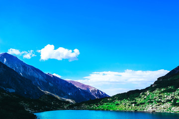 Beautiful alpine lake, river in the high mountains peak, blue sky background. Amazing Mountain hiking paradise landscape, summertime.