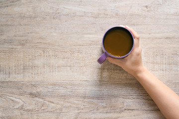 Female hand holding cup of coffee on wood texture background.