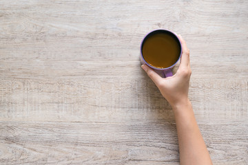 Female hand holding cup of coffee on wood texture background.