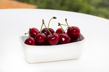 large cherry in a white vase on a white table. Background of a green garden.