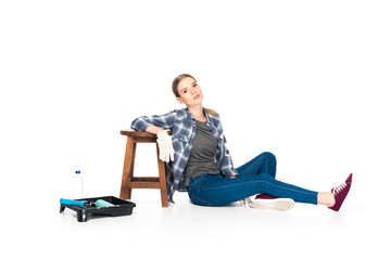 woman sitting on floor near chair, roller tray, paint roller and bottle isolated on white background